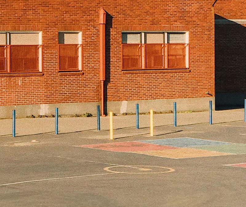 Façade en briques d’un bâtiment public avec une cour asphaltée et des marquages colorés au sol.