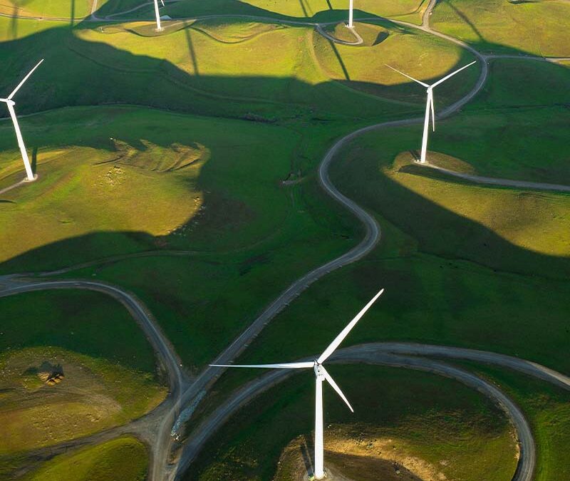 Un vaste champ d’éoliennes implanté sur des collines verdoyantes, captant la force du vent pour générer une électricité propre et continue. Une vision dynamique des énergies renouvelables en mouvement.